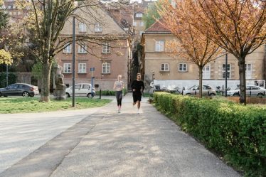 A couple jogging together in an urban park surrounded by greenery and houses.