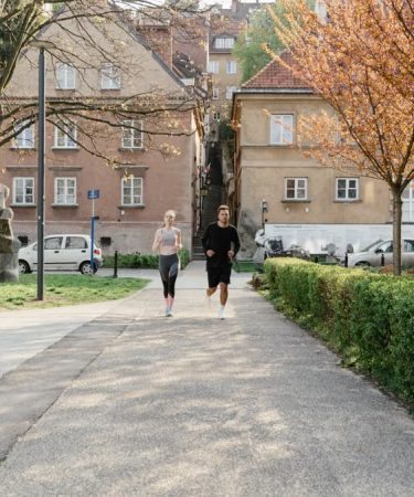 A couple jogging together in an urban park surrounded by greenery and houses.
