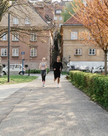 A couple jogging together in an urban park surrounded by greenery and houses.