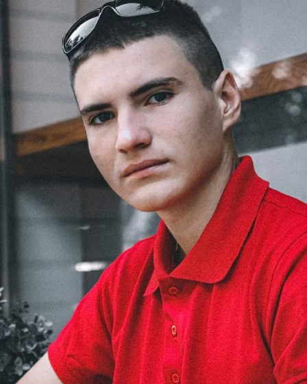 Portrait of a young man wearing a red polo shirt indoors, looking directly at the camera.